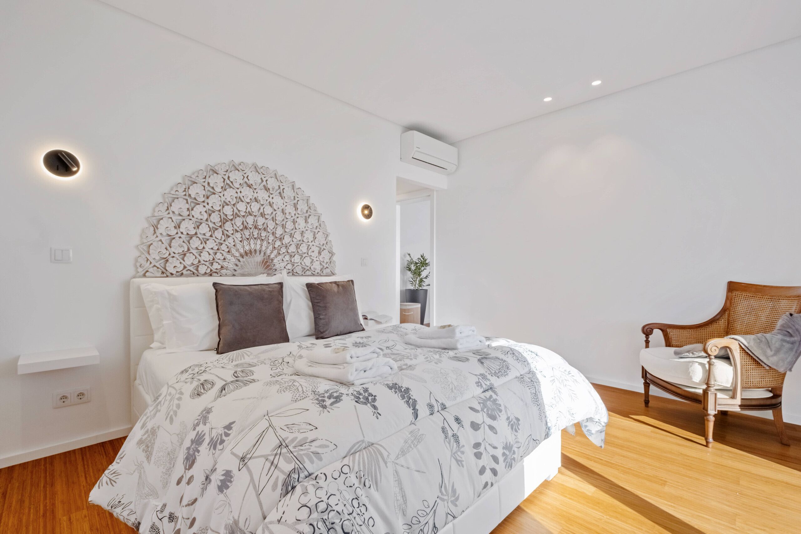 A modern bedroom with a large bed, a decorative wall piece, a wooden chair, and a built-in shelf.