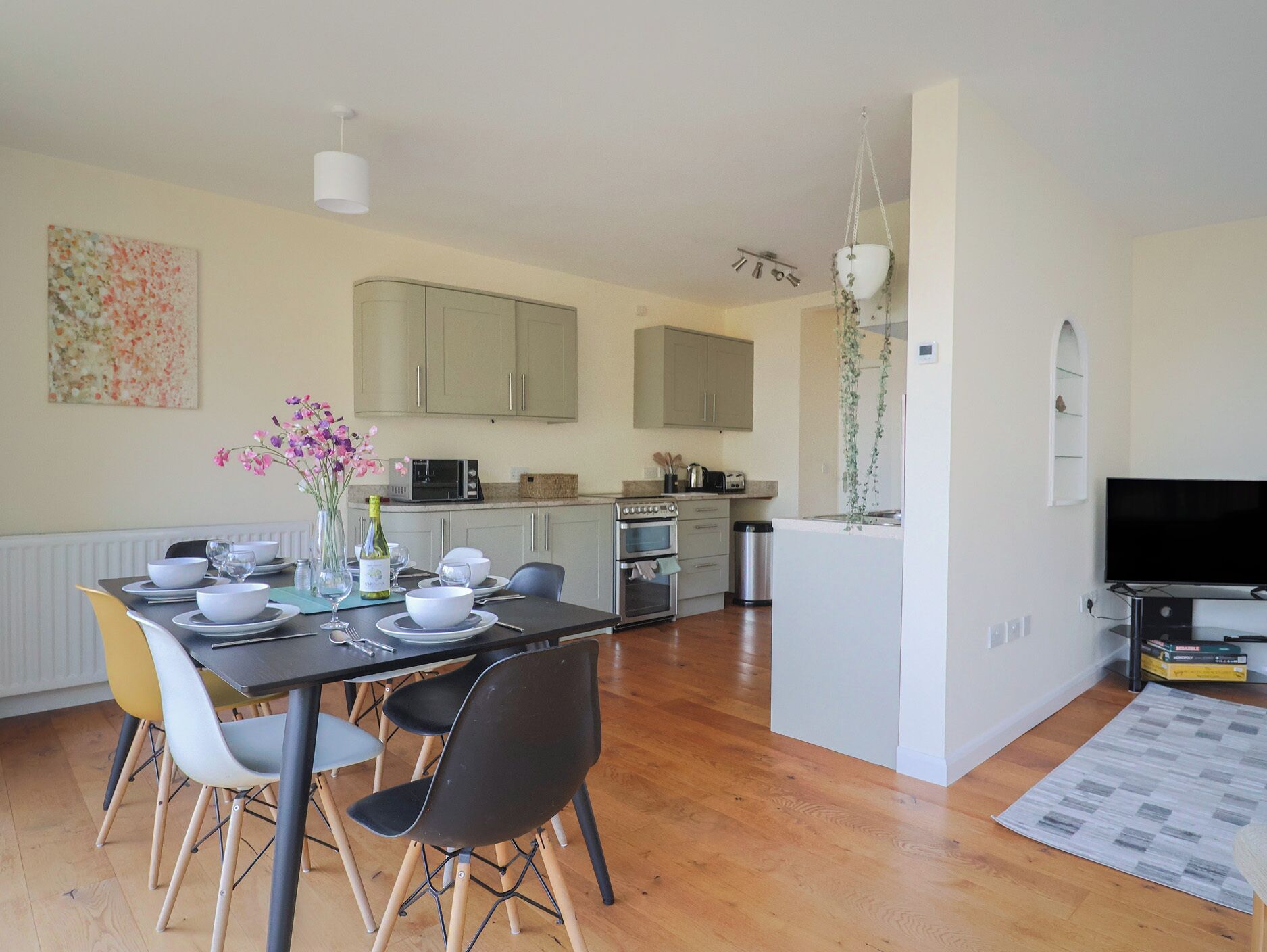 A modern kitchen with white cabinets, a dining table set for four, and a TV in the living area.