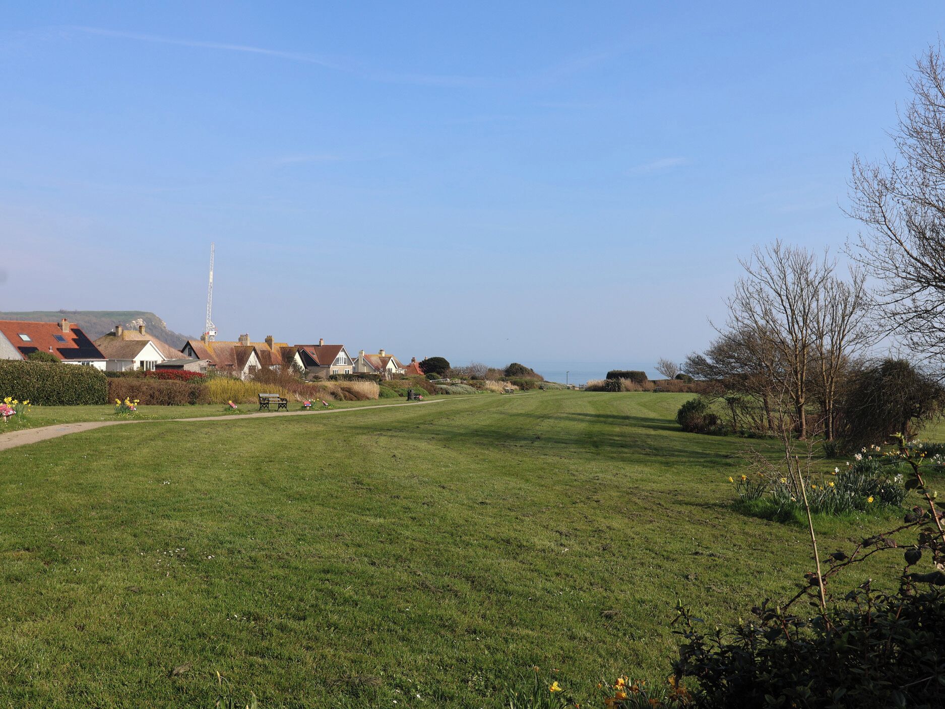 A grassy field with houses, a path, and a distant view of the sea.