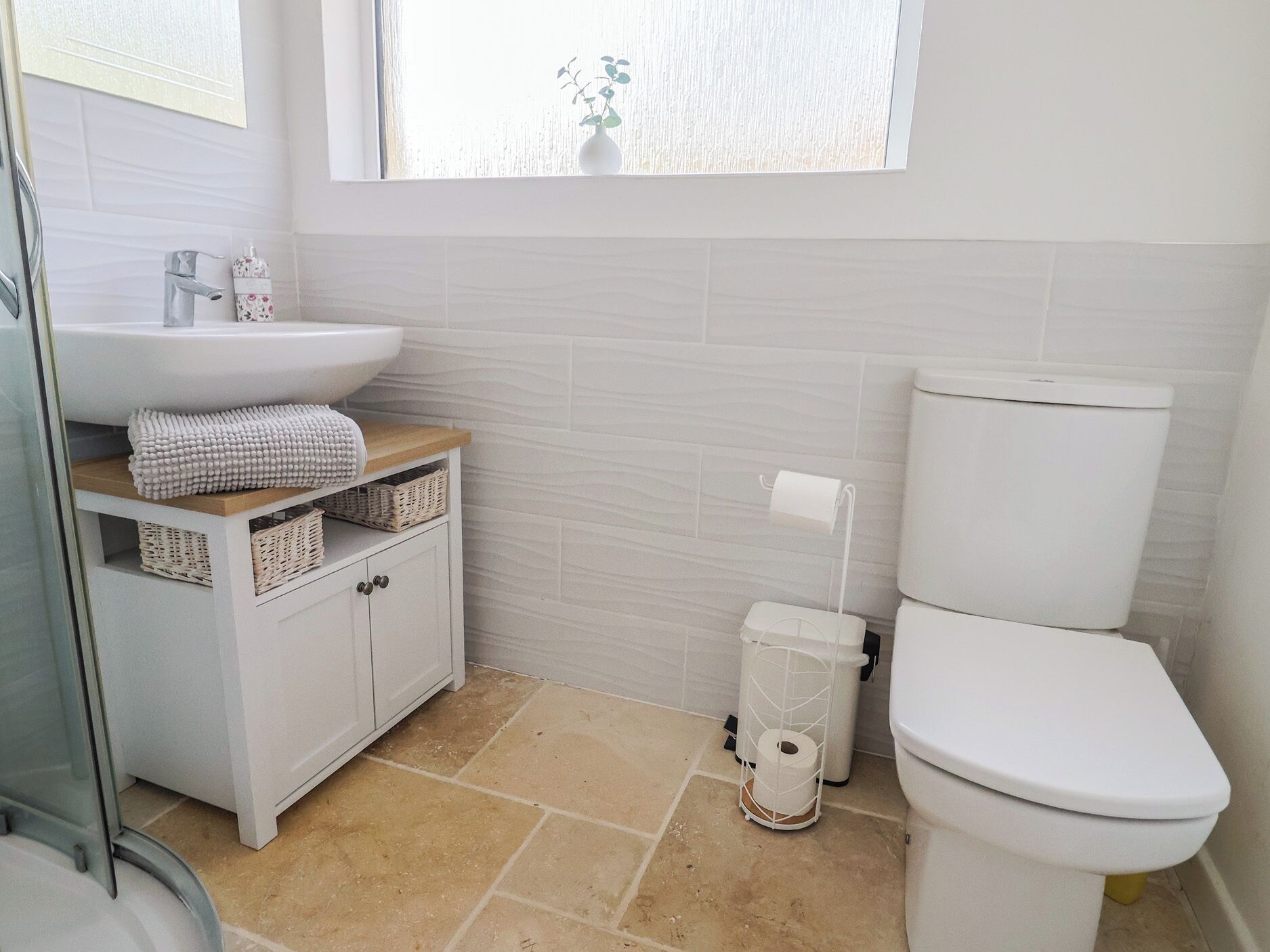 Une salle de bain avec un lavabo blanc, des toilettes et une fenêtre agrémentée d’une plante.