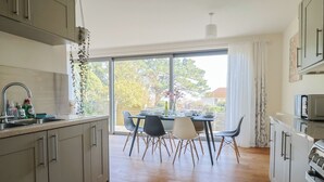 Eine moderne Küche mit Holzausbau, einem Esstisch mit Stühlen und einem großen Fenster mit Blick ins Freie.