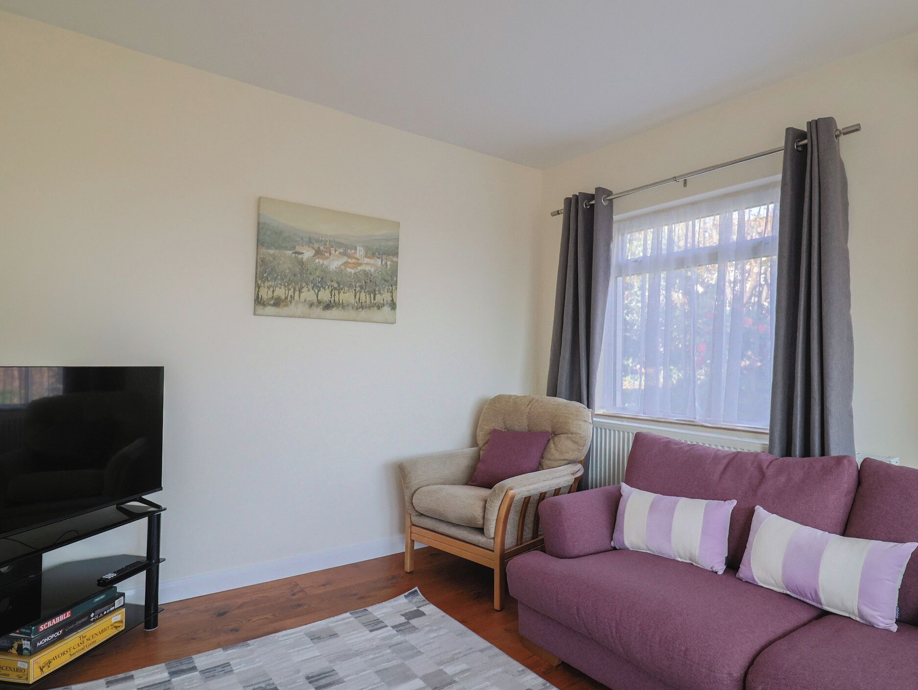 A living room with a television, a sofa, a chair, a painting on the wall, and a window with curtains.
