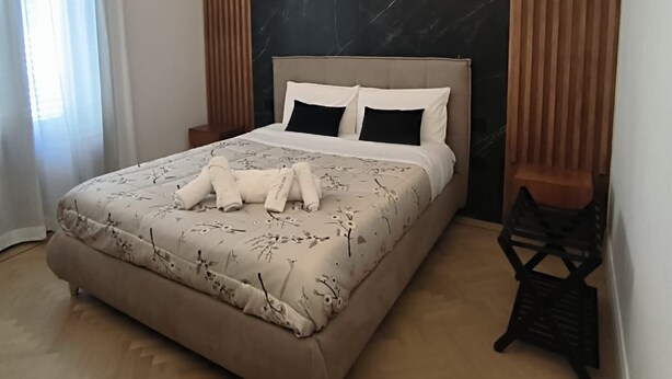 Una cama bien hecha con una colcha floral y dos almohadas, un cabecero de mármol oscuro y suelo de madera.
