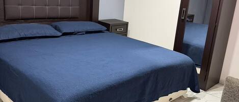 A bedroom with a large bed, a nightstand, a wardrobe, and a mirror.