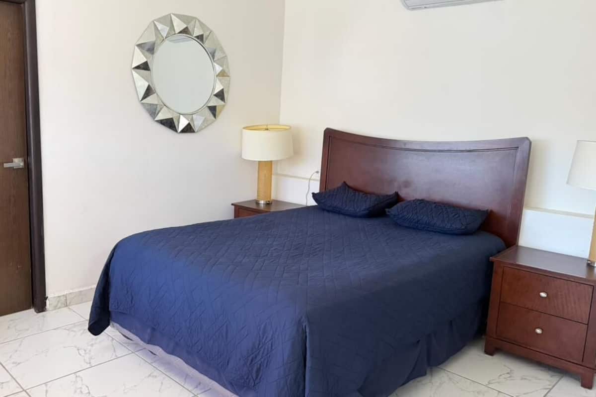 Un dormitorio con una cama, dos mesitas de noche, un espejo y una puerta.