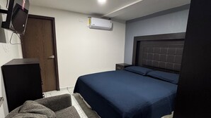 Un dormitorio con cama, televisor montado en la pared, escritorio pequeño y aire acondicionado.