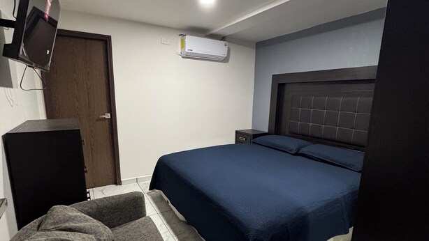 Quarto com cama, televisão na parede, escrivaninha e ar condicionado.