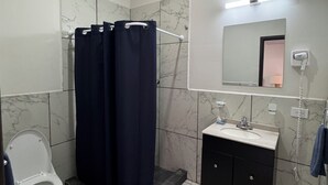 Casa de banho com sanita, chuveiro com cortina, lavatório com espelho e um porta-toalhas.
