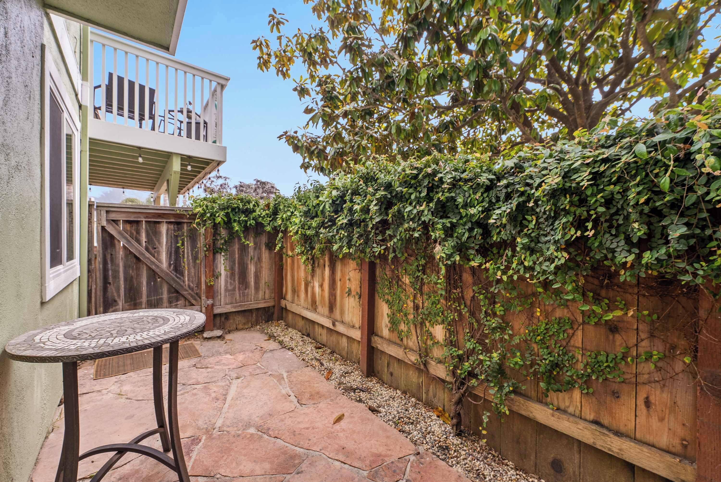 Un espace patio doté d’un sol en pierre, d’une clôture en bois et d’une table dont le plateau est recouvert de mosaïques.