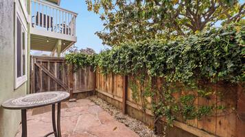 Un espace patio doté d’un sol en pierre, d’une clôture en bois et d’une table dont le plateau est recouvert de mosaïques.