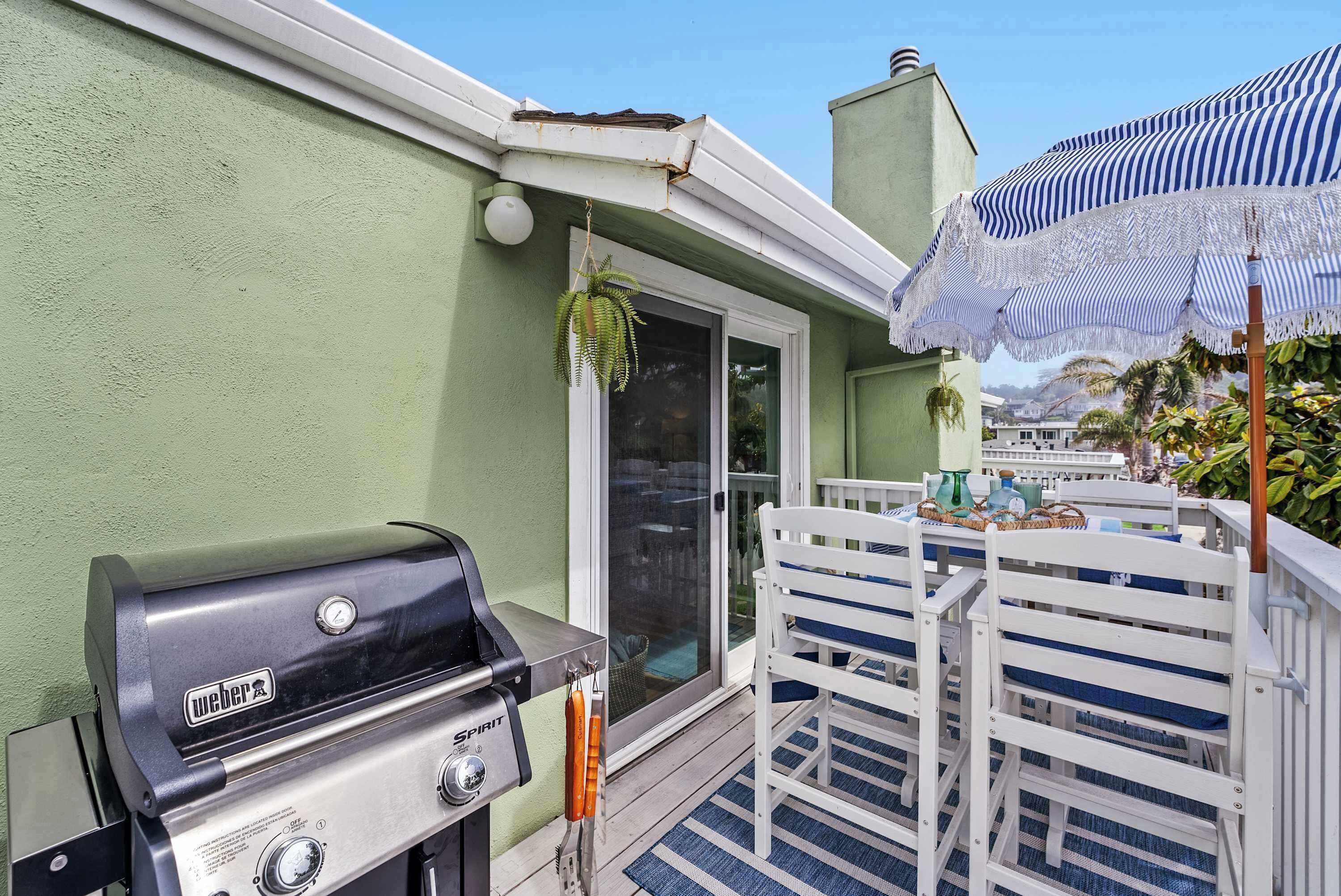 A patio with a Weber Spirit grill, white chairs, and a striped umbrella.