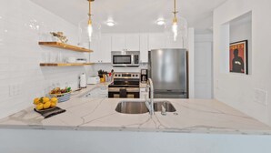 Una cocina moderna con gabinetes blancos, electrodomésticos de acero inoxidable y encimeras de mármol.