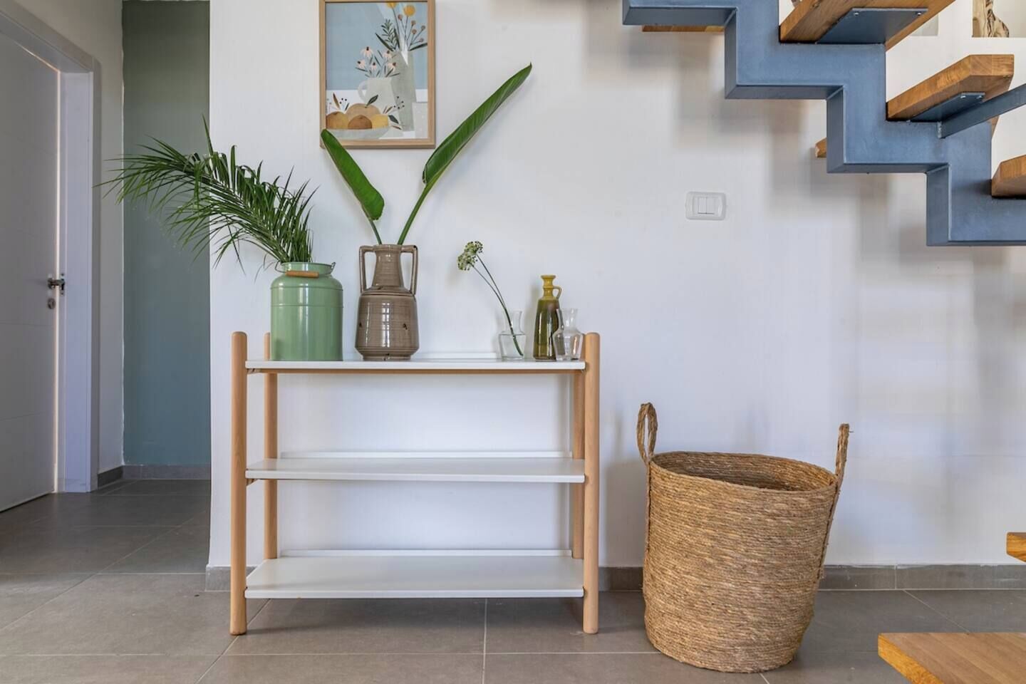 A modern interior with a wooden console table, a woven basket, and a staircase with blue accents.