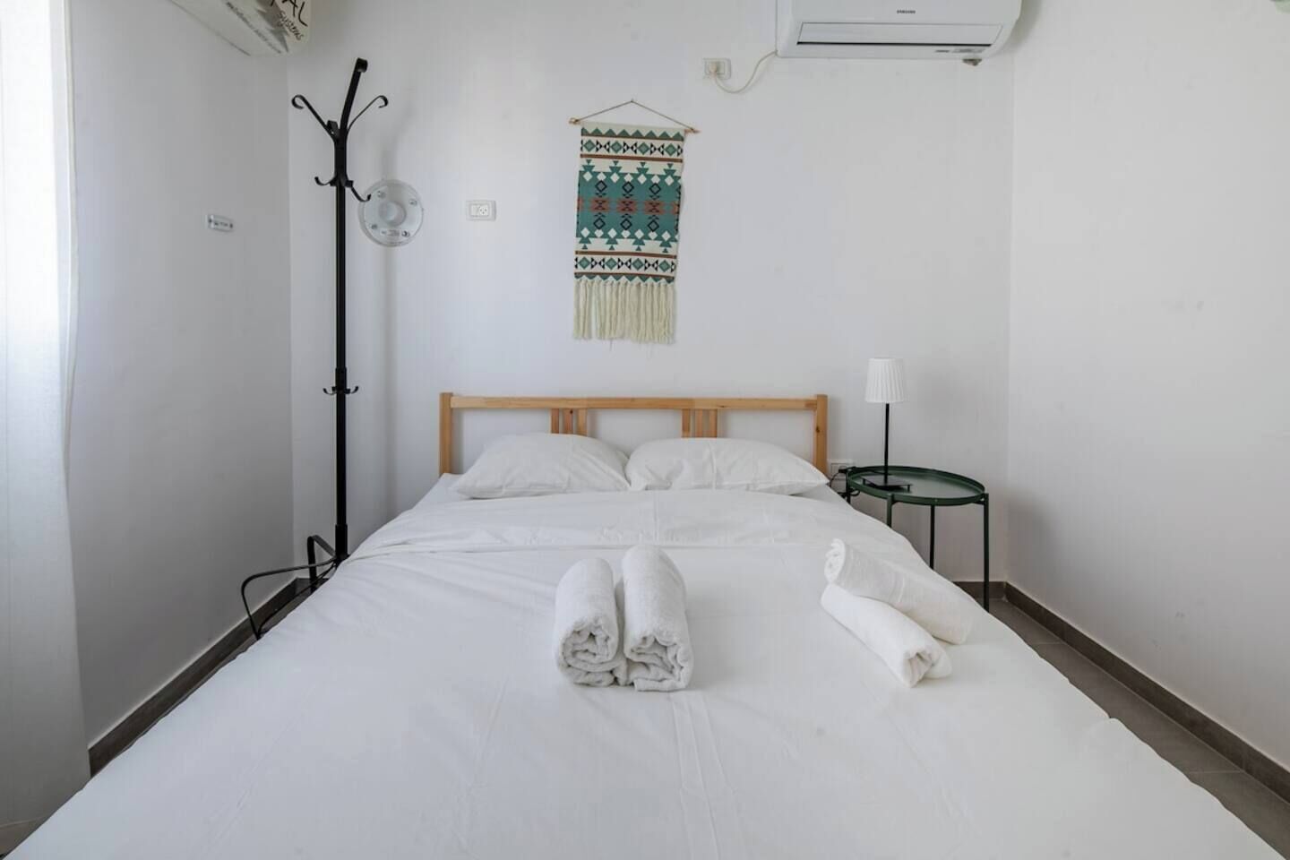 Camera d'albergo con un letto, un comodino con una lampada, un condizionatore d'aria a parete e un arazzo decorativo.