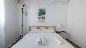 Une chambre d’hôtel comprenant un lit, une table de chevet avec une lampe, un climatiseur fixé au mur et une tapisserie décorative.
