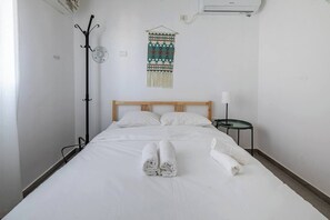 Ein Hotelzimmer mit einem Bett, einem Nachttisch mit Lampe, einer Wand-Klimaanlage und einem dekorativen Wandteppich.