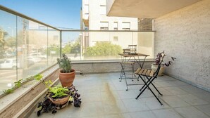 Un balcon avec une table et des chaises, des plantes en pot et une vue sur la rue.