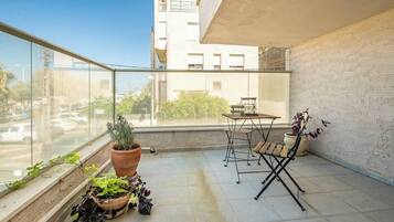 A balcony with a table and chairs, potted plants, and a view of the street.