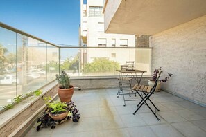 Ein Balkon mit Tisch und Stühlen, Blumentöpfen und Blick auf die Straße.