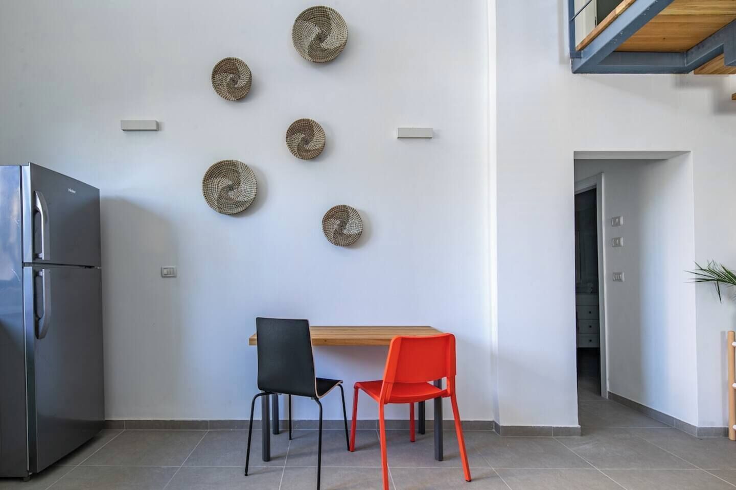 A modern kitchen with a stainless steel refrigerator, a wooden dining table, two chairs, and decorative wall art.