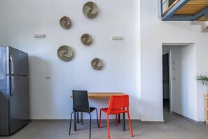Una cocina moderna con un refrigerador de acero inoxidable, una mesa de comedor de madera, dos sillas y decoración en la pared.