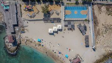An aerial view of a beach with a basketball court, umbrellas, and a parking lot.