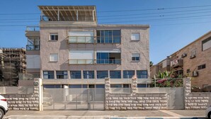 Un immeuble à plusieurs étages doté d’une entrée sécurisée par un portail, d’un toit plat recouvert de panneaux solaires et d’une façade en briques.