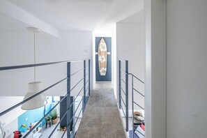 Een smalle gang met een betonnen vloer, metalen leuning en een plafondlamp.