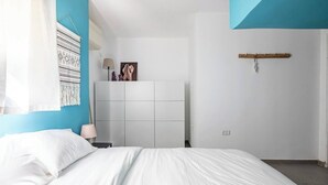 Une chambre à coucher comprenant un lit, une table de chevet, une armoire fixée au mur et une porte.