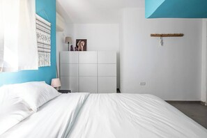 Um quarto com uma cama, uma mesa de cabeceira, um guarda-roupa fixado na parede e uma porta.