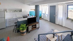 Une cuisine moderne avec des meubles blancs, un coin repas agrémenté d’un tapis bleu et un espace de vie avec un canapé et un téléviseur.