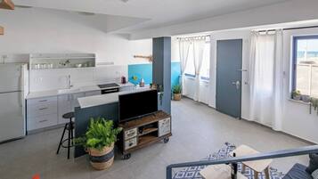A modern kitchen with white cabinets, a dining area with a blue rug, and a living space with a sofa and a TV.