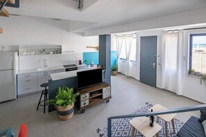 Uma cozinha moderna com armários brancos, uma área de jantar com tapete azul e um espaço de estar com sofá e televisão.