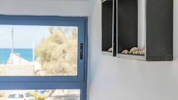 A room with a view of the sea through a window, a door, and a wall-mounted shelf with seashells.