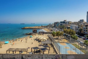 Uma praia com areal, um cais e um horizonte urbano ao fundo.
