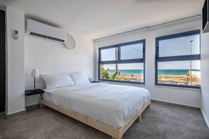 A bedroom with a bed, a nightstand, a lamp, and a view of the beach through large windows. - Port city - beachfront 5 bdrms apartment+ mamad (Haifa)