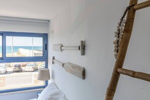 A room with a bed, a window with a view of parked cars and a beach, and a wall with three wooden bathtubs. - Port city - beachfront 5 bdrms apartment+ mamad (Haifa)