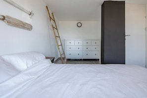 Un dormitori amb un llit, una petxera, una escala i una porta.