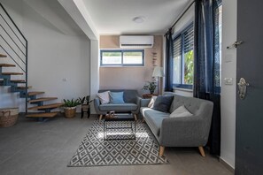 Ein modernes Wohnzimmer mit einem grauen Sofa, einem gemusterten Teppich, einer Treppe mit Holzdielen und einem Fenster mit Vorhängen.