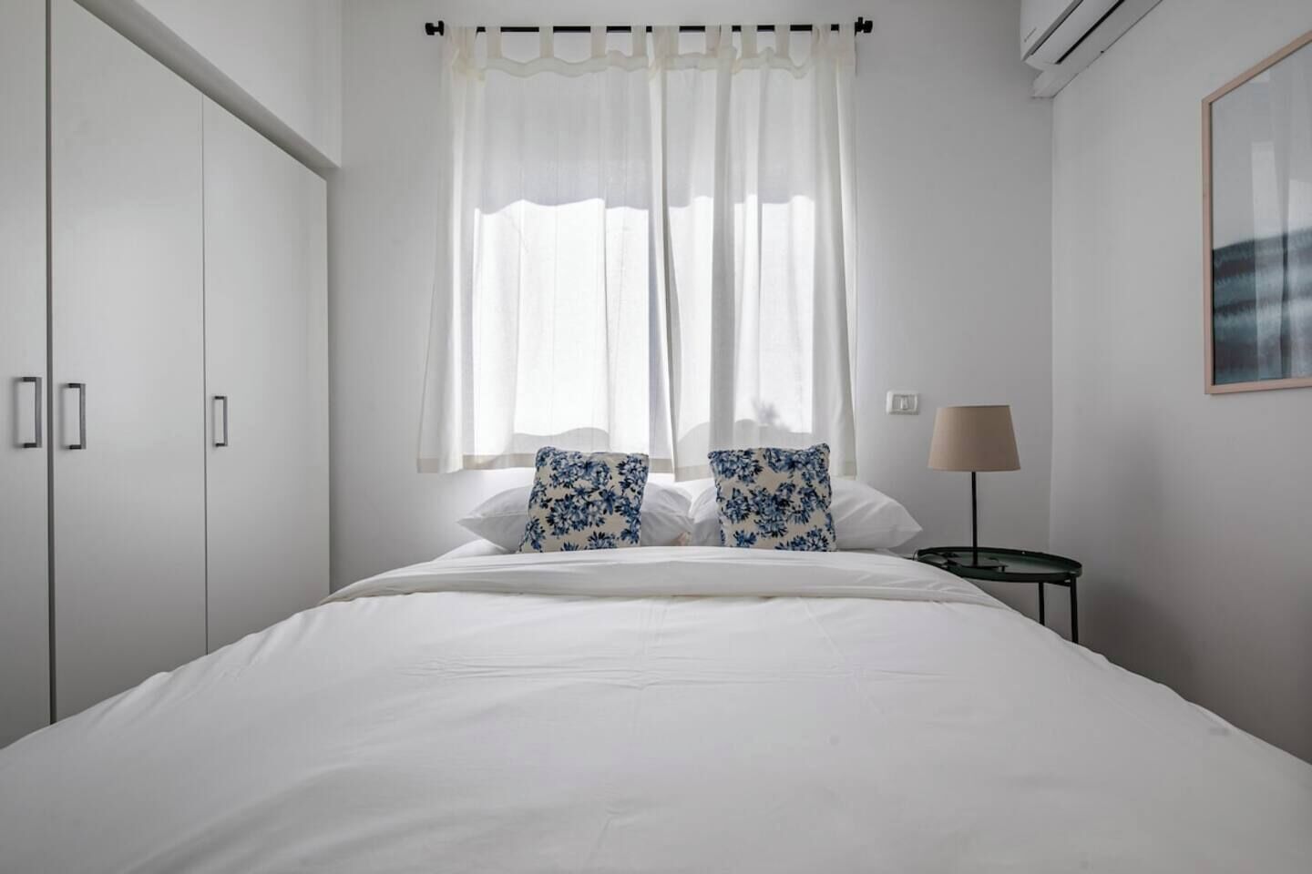 A bedroom with a bed, two pillows, a nightstand, a lamp, and a wardrobe.