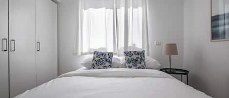 A bedroom with a bed, two pillows, a nightstand, a lamp, and a wardrobe.