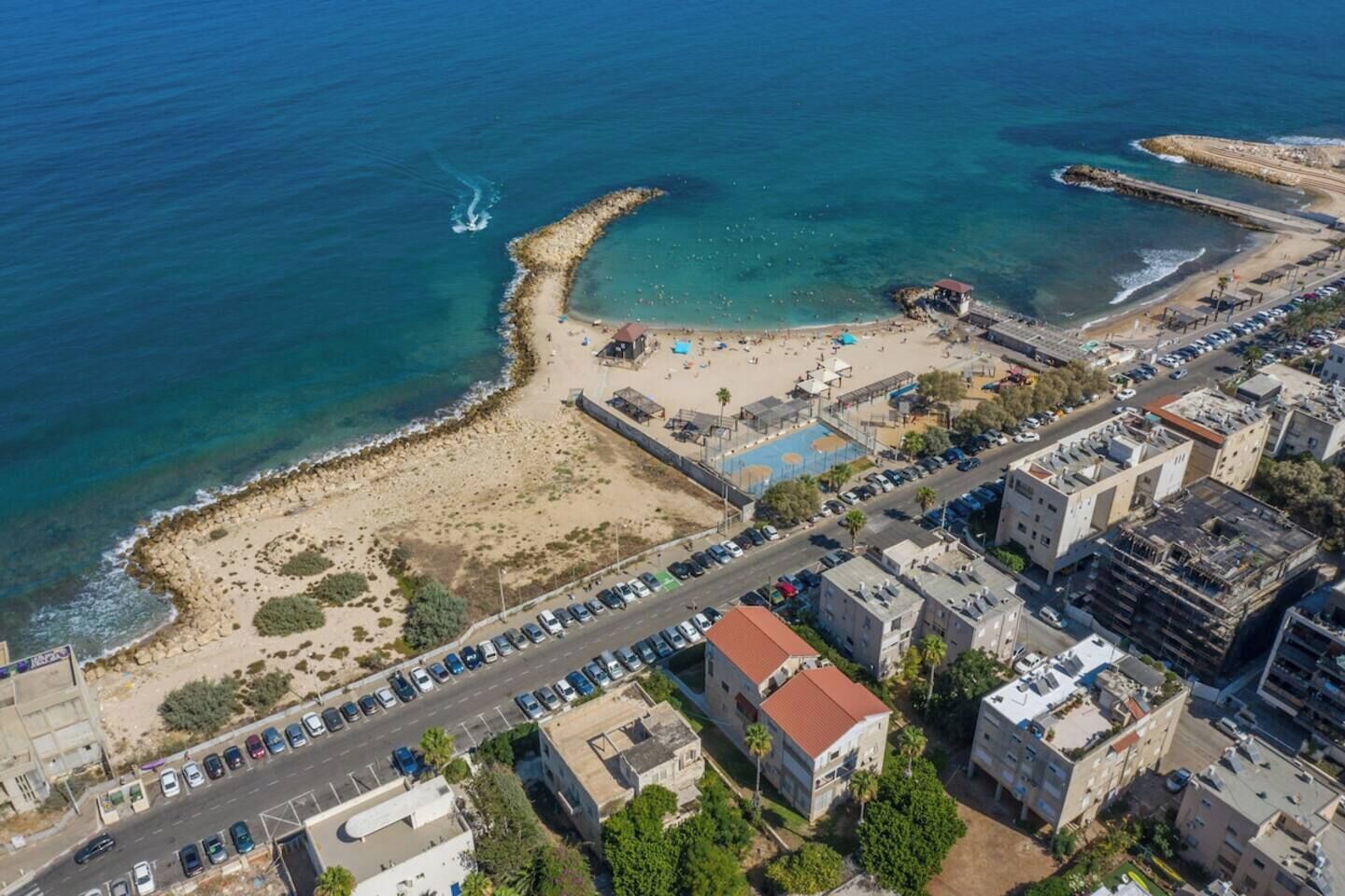 Vista aèria d'una zona costera amb una platja, aparcaments i edificis.
