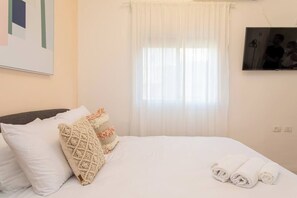 A hotel room with a bed, white bedding, a window with sheer curtains, and a framed picture on the wall. - Port city haifa-studio w/ balcony near the beach 2 (Haifa)