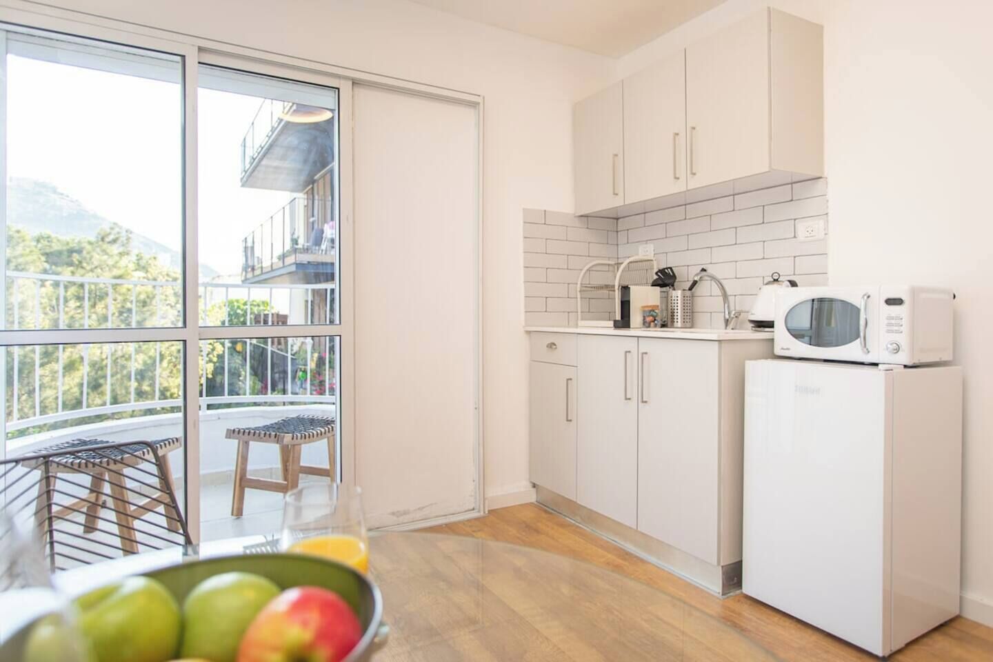Une cuisine avec des meubles blancs, un four à micro-ondes et un réfrigérateur. Une fenêtre offre une vue sur la verdure à l’extérieur.