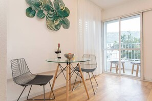A dining area with a glass table, two chairs, a bottle of wine, and a bowl of fruit. - Port city haifa-studio w/ balcony near the beach 2 (Haifa)