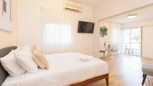 Una habitación de hotel con cama, televisión, zona de comedor y balcón.