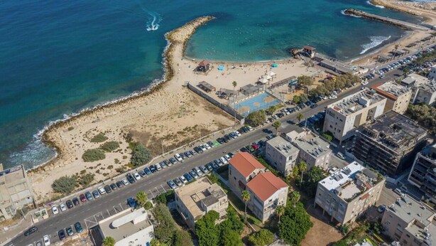 Vista aérea de una zona costera con playa, estacionamiento y edificios.