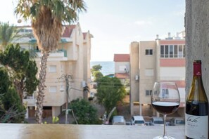 Un got de vi i una ampolla a un balcó amb vista a una zona residencial i un cel clar.