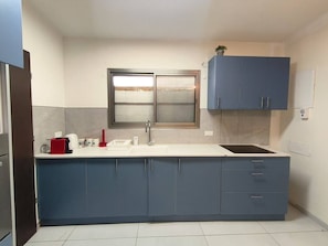 A kitchen with a white countertop, blue cabinets, a window above the sink, and a small plant on the cabinet. - Port city haifa - 1 bdrm apt Near beach 2 (Haifa)