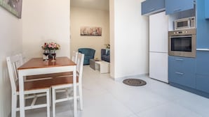 A modern kitchen with blue cabinets, a built-in oven, and a dining area with a wooden table and white chairs. - Port city haifa - 1 bdrm apt Near beach 2 (Haifa)